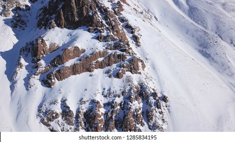 Huge rocks covered with snow. Ledges from the snowy mountains. Cliffs and large rocks. Dangerous terrain. Drone view from the top and side. The sun's rays on the Shadow of the mountains. - Powered by Shutterstock