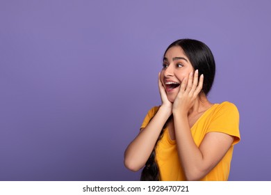 Huge Sale Or Promo Concept. Amazed Indian Woman Screaming And Touching Her Face In Disbelief, Looking At Free Copy Space On Purple Studio Background. Astonished Young Lady With Open Mouth