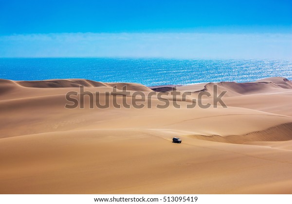 Huge\
sand dunes moving on the Atlantic coast. Sandwich Harbour - part of\
Namib-Naukluft National Park. Tourist trip by\
jeep