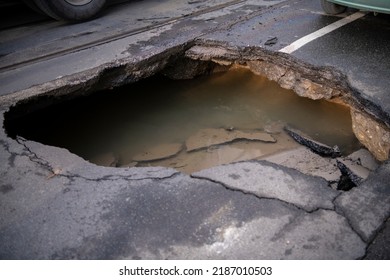 Huge Sinkhole On Busy Asphalt Road Surface On Which Cars Drive. Accident Situation On A City Street Due To Cracks In Asphalt. Broken Hole Filled With Muddy Water.
