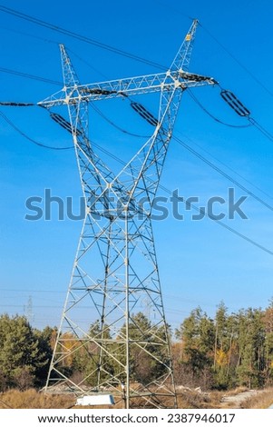 A huge steel electric pole - a high-voltage line against a blue sky in the forest.A high-height steel truss electric pole standing in a pine forest and carrying a large amount of transmission cables.