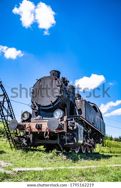 Huge vintage steam locomotive, black and red\
painted steel train. Coal-powered steam express stands on tracks.\
Classic gigantic heavy railway machinery. Side view of power parts\
of machine.