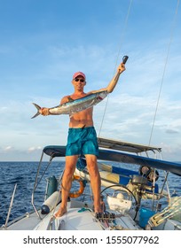 Huge Wahoo (spanish mackerel, king fish) trolling on a sailing yacht. Happy fisherman in shorts with his trophy on background of white boat deck. Fishing in Indian ocean near Phuket island, Thailand