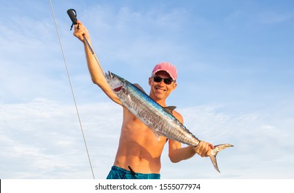 Huge Wahoo (spanish mackerel, king fish) trolling on a sailing yacht. Happy fisherman in shorts with his trophy on background of white boat deck. Fishing in Indian ocean near Phuket island, Thailand