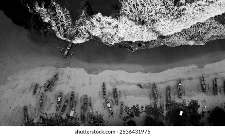 Huge waves crash into the shores of Sawarna, Banten, Indonesia, leaving a trail of white foam, while fishing boats lined up on the sand await their turn to go out to sea in this black and white photo. - Powered by Shutterstock