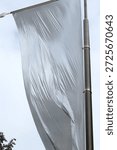 Huge white flag dancing in the wind. Air current blowing and moving the drapery. Fabric gets wrinkles through the movement. Hung high up in Paris, France in a public place. Shot low angle.