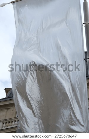 Huge white flag dancing in the wind. Air current blowing and moving the drapery. Fabric gets wrinkles through the movement. Hung high up in Paris, France in a public place. Shot low angle.
