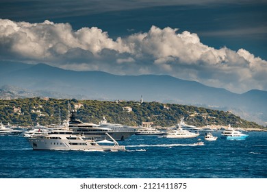 A lot of huge yachts are in harbour near port Hercules of Monaco at sunny day, megayachts are moored in sea, is a yacht show, Monte Carlo, island is on background, glossy board of the megayachts