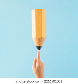 A huge yellow wooden pencil standing the index finger child's hand against pastel blue background  Minimal abstract school concept easy handwriting drawing exercises  Education idea 