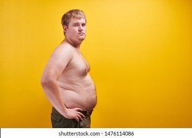 Huge Young Man With Big Fat Belly And Naked Body In Profile. Concept Of Obesity, Fast And Junk Food, Sports, Liposuction, Weight Loss With Free Space For Your Product Or Text