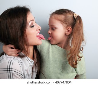 Hugging funny mother and daughter quarreling and showing each other the tongues. Closeup humor portrait