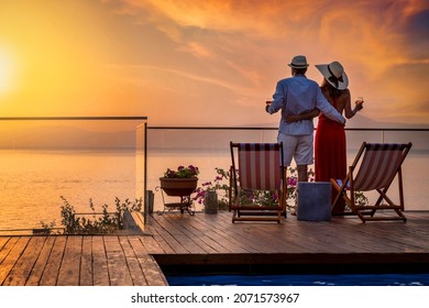 A hugging holiday couple enjoys the beautiful summer sunset over the mediterranean sea with a glass of wine - Shutterstock ID 2071573967