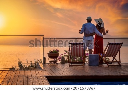 A hugging holiday couple enjoys the beautiful summer sunset over the mediterranean sea with a glass of wine