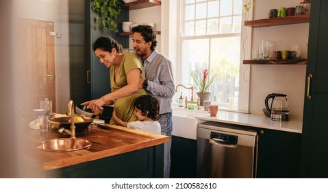 Hugging mom in the kitchen. Cheerful father and son giving playful hugs to mom while she prepares breakfast. Happy ethnic family spending some quality time together at home. - Powered by Shutterstock
