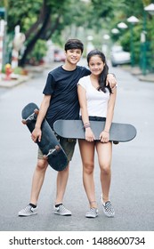 Hugging Teenage Brother And Sister Standing In The Street With Skateboards In Hands