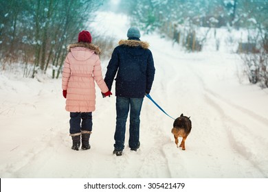 Hugging young couple in love walking with dog outdoors in snowy winter