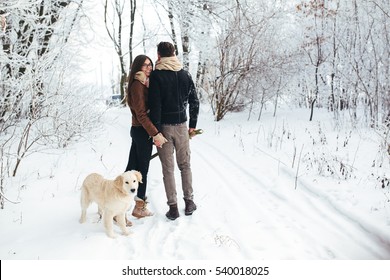 Hugging young couple in love walking with dog outdoors in snowy winter