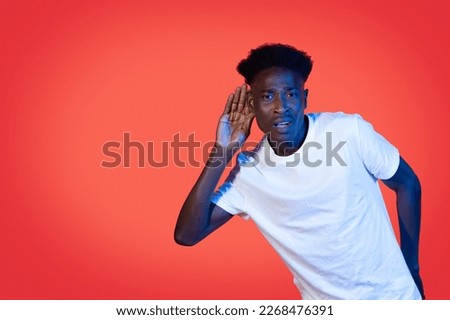Huh, What Did You Say. African American Guy Listening Holding Hand Near Ear Over Red Studio Background In Neon Light, Looking At Camera. Man Making Dont Hear You Gesture. Speak Up, Overhearing
