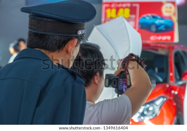 Huizhou, China - MAR 2019: The photographer\
is shooting the unidentified female model posed for photograph with\
the new car by Toyota, and security guard peeked at the camera\
behind the\
photographer.