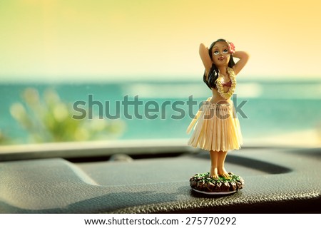 Hula dancer doll on Hawaii car road trip. Doll dancing on the dashboard in front of the ocean. Tourism and Hawaiian travel freedom concept.