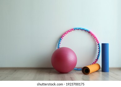 Hula hoop, fitness ball and mats near light wall in gym. Space for text