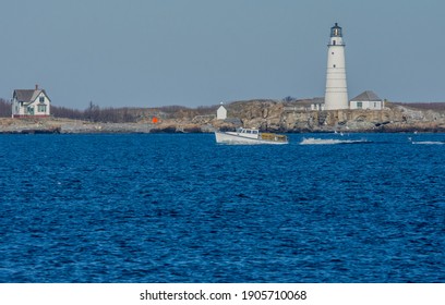 Hull, MA USA-Nov. 29, 2020: A Lobster Boat Filled With Traps Cruises The Ocean In Front Of Boston Light Located On The Rocky Little Brewster Island In Boston Harbor With A Lighthouse Keeper's House. 