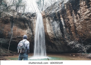 Human with backpack standing by the waterfall and looking at it. Cold weather, fall hiking. Wanderlust photo series.