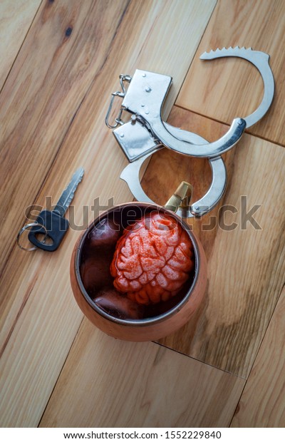 Human brain\
in copper Moscow mule cocktail mug soaking with car keys and\
handcuffs for alcoholism addiction concept\
