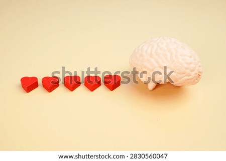 Human brain model with five red hearts on yellow background, representing emotional intelligence, mental wellness, self love, positive thinking and psychological health.