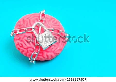 Human brain model surrounded by chains and secured with a padlock on blue background with copy space. Mental imprisonment related concept.