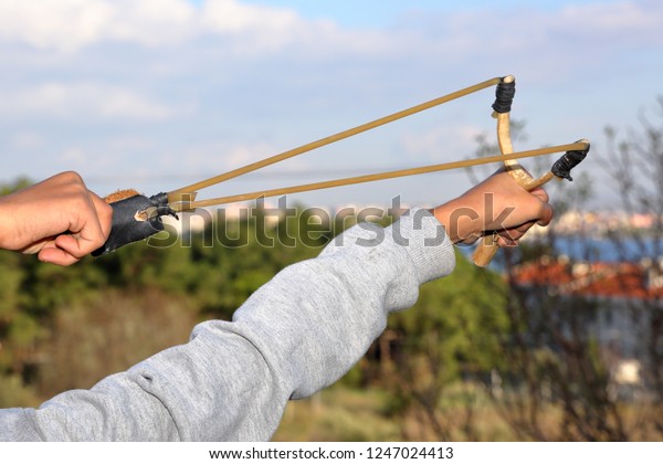 human\
(child) is throwing stone with slingshot - wooden slingshot with a\
stretched rubber band. slingshot is ready to\
fire