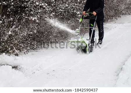 Human cleans snow off path with wireless electric snow blower after the winter snowfall