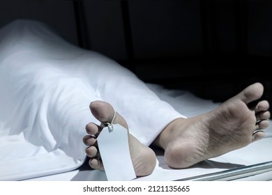 Human corpse covered with a sheet and name tag on toe in the morgue - Shutterstock ID 2121135665