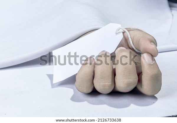 Human corpse covered with a sheet and name tag on\
hand in the morgue