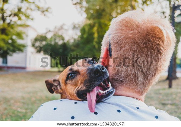 Human and dog friendship: young man hugs\
his funny dog, person\'s back perspective. Smiling puppy with floppy\
ears and tongue interacting with her\
owner