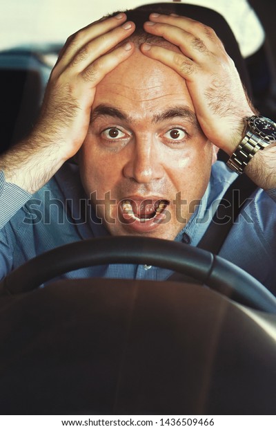 Human emotion face expression.\
Man driving a car shocked about to have traffic accident,\
windshield view. Scared funny looking young man driver in the car.\
Toning