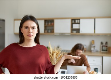 Human Emotions And Feelings. Angry Young Dark Haired Woman Making Indignant Gesture With Hand, Frowning, Being Annoyed With Husband Who Is Ignoring Her, Working All Day Long On His Laptop