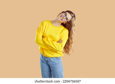 Human Emotions. Portrait Of Cheerful And Goofy Girl With Wide Funny And Crazy Smile On Light Beige Background. Young Woman In Jeans, Sweatshirt And Glasses Posing With Funny Grimace On Her Face.