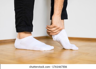 menschliche Füße, die auf Holzfußboden stehende weiße Knöchelsocken von Hand aufsetzen