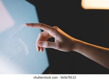 Human finger pointing on the glowing computer screen with blue and blur effects flare side view close-up