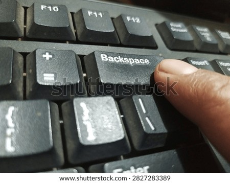 Human finger pressing the Backspace key on a black desktop computer keyboard. Concept of undoing mistake, error correction, editing text, typing, and digital revision.