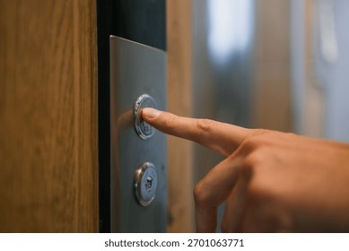 Human finger pressing silver elevator call button, signaling a wait for vertical transportation in a modern building, representing movement and transition