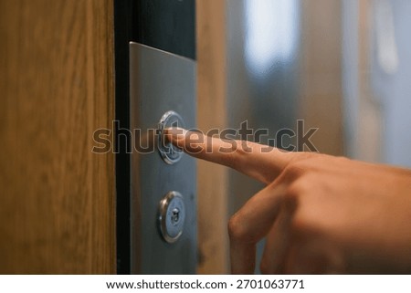 Human finger pressing silver elevator call button, signaling a wait for vertical transportation in a modern building, representing movement and transition