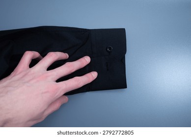 Human hand buttoning black button on cuff of black shirt on gray background.