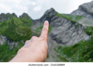 Human hand close-up pointing finger at the top of mountain range covered with green grass hiking and climbing concept summit ascent