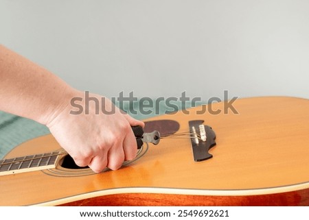 human hand cutting old strings with pliers to remove pegs or pins from guitar bridge and replace old strings on acoustic guitar