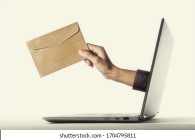 The human hand with envelope stick out of a laptop screen. Concept of correspondence, feedback, advertising via internet. - Shutterstock ID 1704795811