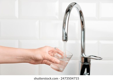 Human hand filling glass with fresh pure drinkable tap water from faucet in white kitchen, banner with concept of natural clean aqua at home, banner with copy space - Powered by Shutterstock