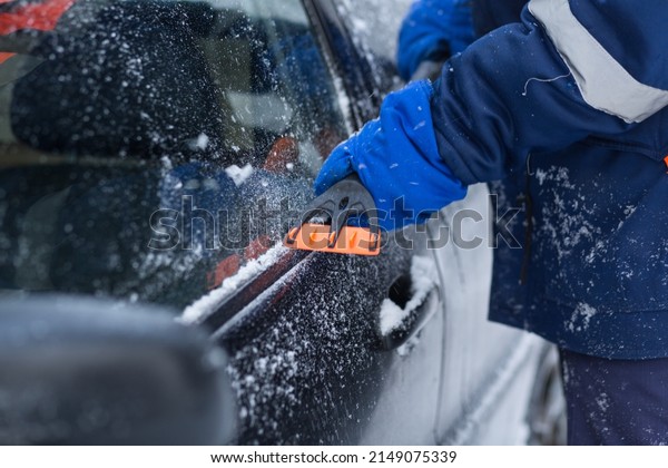 A human hand in a\
glove cleans a blue car from snow with a special brush. A hand\
sweeps snow from the hood of the car. Horizontal photo. the\
consequences of a blizzard
