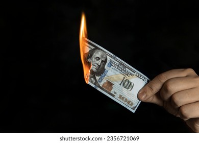 Human hand holding a burning 100 dollar bill. concept of inflation, a decrease in the purchase of foreign currency, and devolution. - Powered by Shutterstock